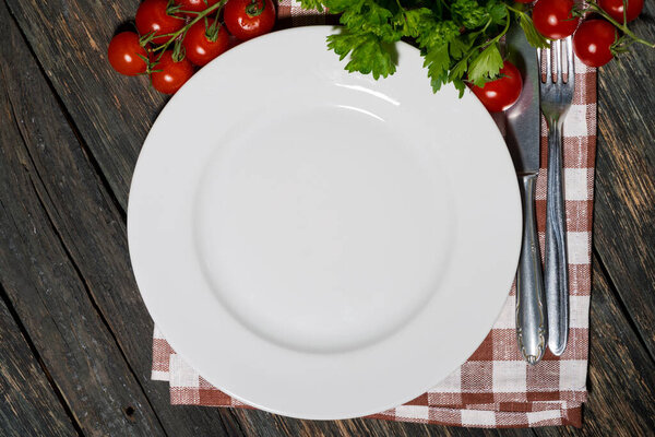 table setting with white plate and vegetables on wooden table, top view horizontal