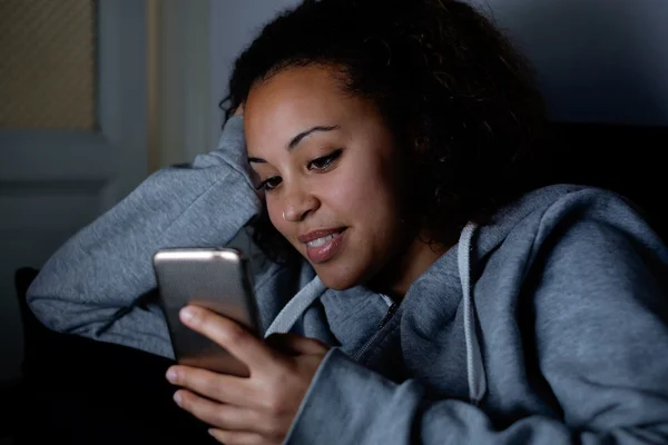 Jovem usando seu celular à noite no sofá — Fotografia de Stock