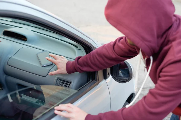 Ladrón encapuchado robando un teléfono móvil de un coche aparcado —  Fotos de Stock