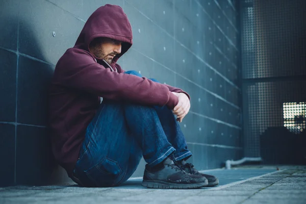 Desesperado hombre solitario sentado contra la pared en la calle de la ciudad — Foto de Stock