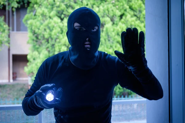 Ladrão usando uma balaclava olhando pela janela da casa — Fotografia de Stock