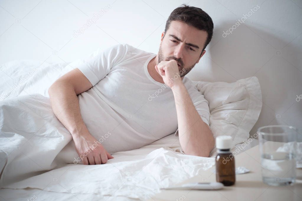 Man feeling bad lying in the bed and looking the thermometer