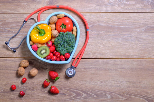 Heart shaped dish with vegetables and stethoscope isolated on wo