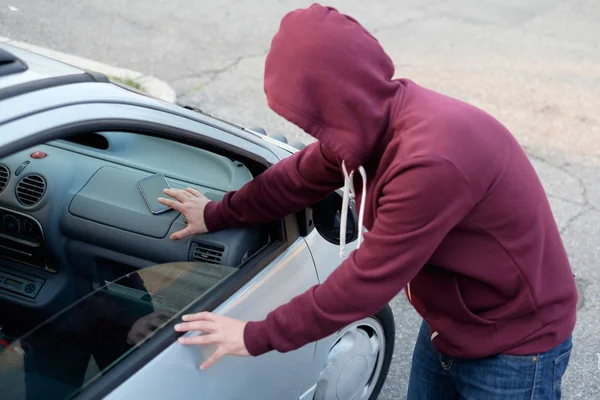 Ladrón encapuchado robando un teléfono móvil de un coche aparcado —  Fotos de Stock
