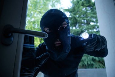 Burglar wearing a balaclava looking through the house window clipart