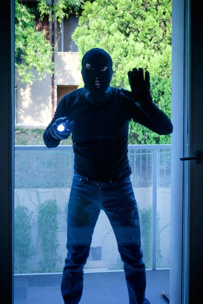 Ladrão usando uma balaclava olhando pela janela da casa — Fotografia de Stock