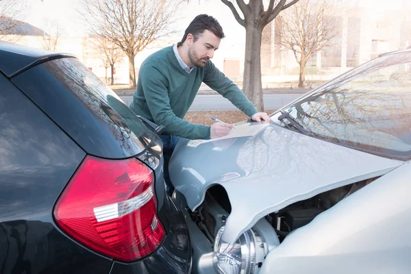 Man writing a car insurance claim after a car crash — Stock Photo, Image