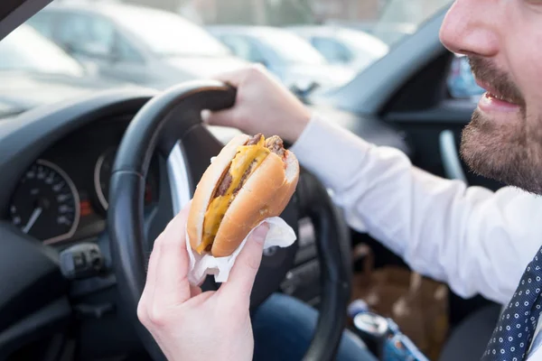 Hombre comiendo una hamburguesa mientras conduce su coche — Foto de Stock