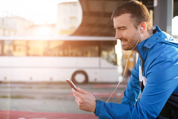 Ο άνθρωπος περιμένει στο σταθμό λεωφορείων και να ακούτε μουσική στο κινητό — Φωτογραφία Αρχείου
