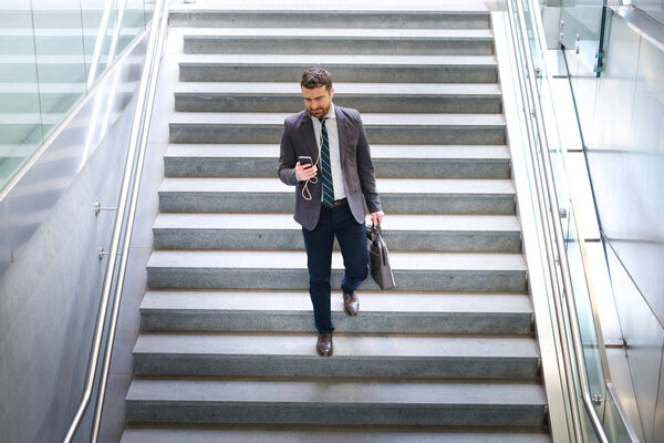 Businessman is looking at his mobile phone while is going to wor