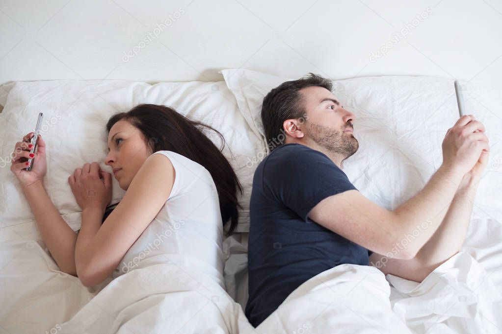 Bored lovers couple in bed and using  mobile phones 