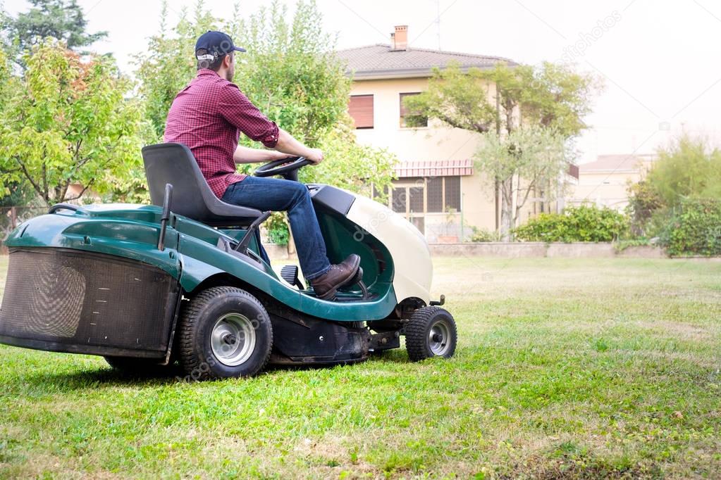 Gardener cutting the grass of a garden seated on lawn mower