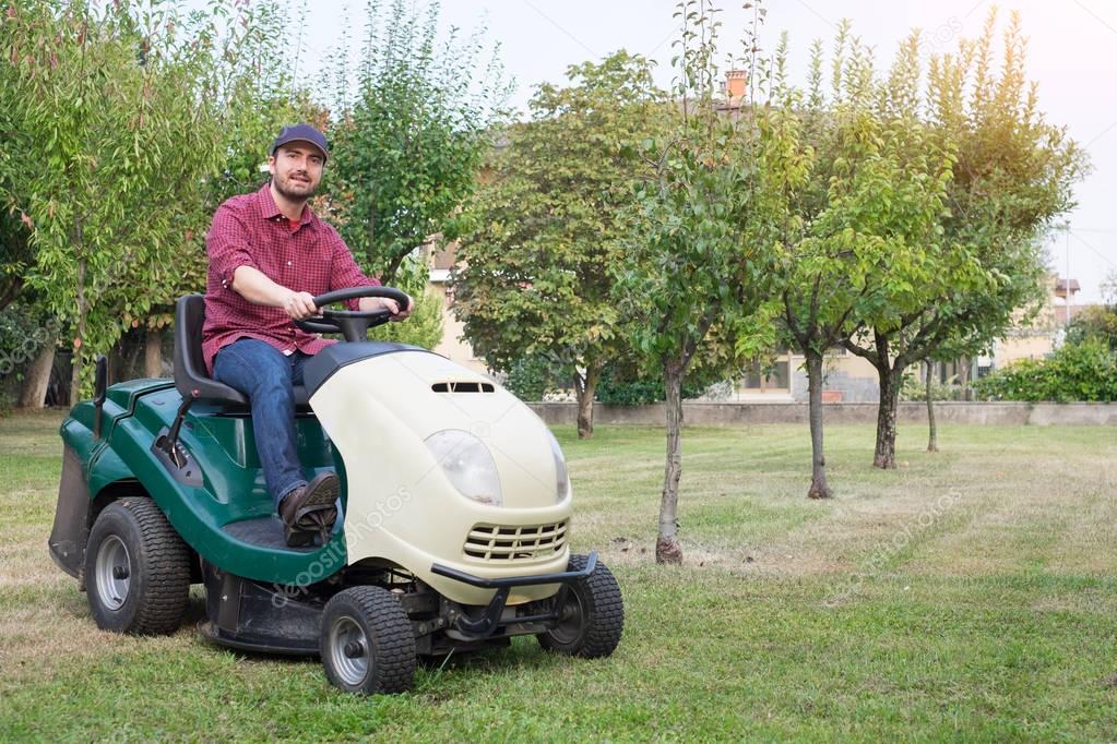 Gardener cutting the grass of a garden seated on lawn mower