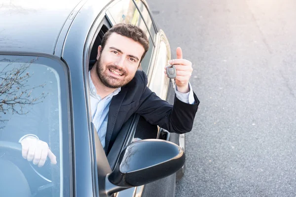 Homme heureux souriant assis dans sa voiture tenant la clé — Photo