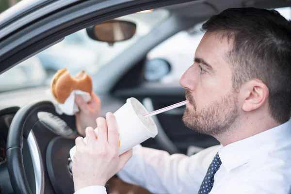 Hombre comiendo una hamburguesa y conduciendo sentado en coche — Foto de Stock