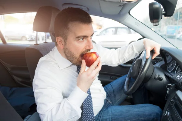 Hombre comiendo una manzana conduciendo coche — Foto de Stock