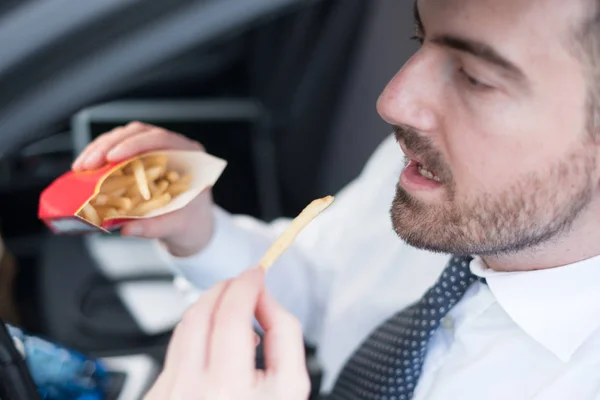 Hombre comiendo comida chatarra y conduciendo sentado en el coche —  Fotos de Stock