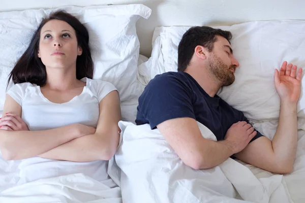 Triste e atenciosa mulher acordada enquanto o marido dorme na cama — Fotografia de Stock