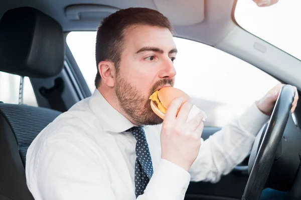 Hombre comiendo una hamburguesa y conduciendo sentado en coche — Foto de Stock