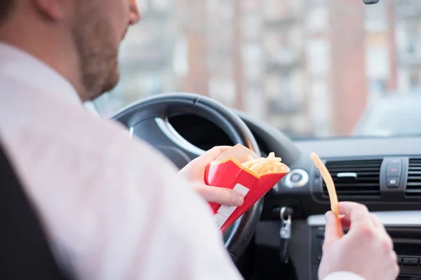 Hombre comiendo comida chatarra y conduciendo sentado en el coche — Foto de Stock