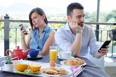 Kahvaltı saati sırasında akıllı telefon kullanarak sıkılmış Çift