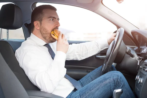 Hombre comiendo una hamburguesa y conduciendo sentado en coche — Foto de Stock