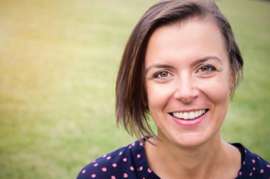 Bir parkta gülümsemeyle gülümseyerek ve kameraya arayan kadın