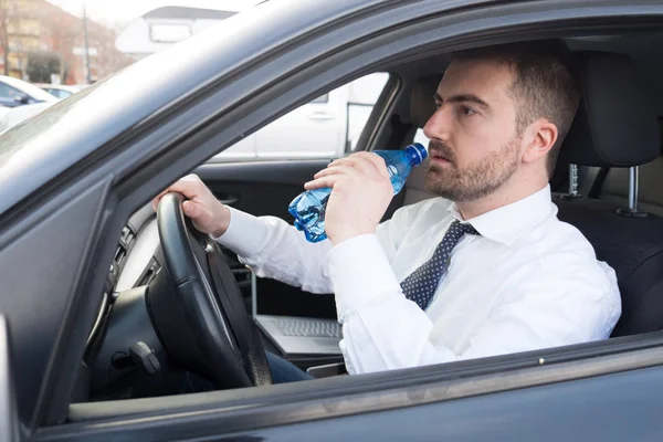Человек пьет воду, сидя в машине — стоковое фото