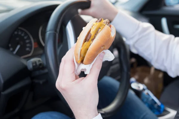 男性が車を運転中、ハンバーガーを食べて — ストック写真