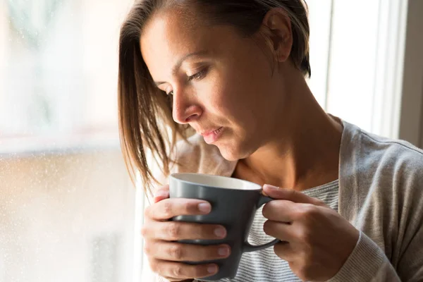 Woman holding a cup of coffee portrait next to a window — Stock Photo, Image