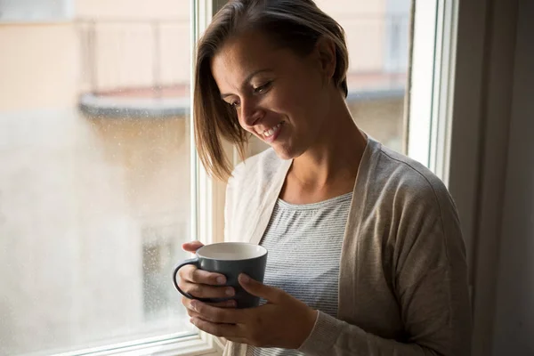 Relaxed woman holding a cup of coffee portrait next to a window — Stock Photo, Image