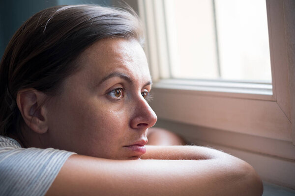 Sad woman portrait next to a window looking outside