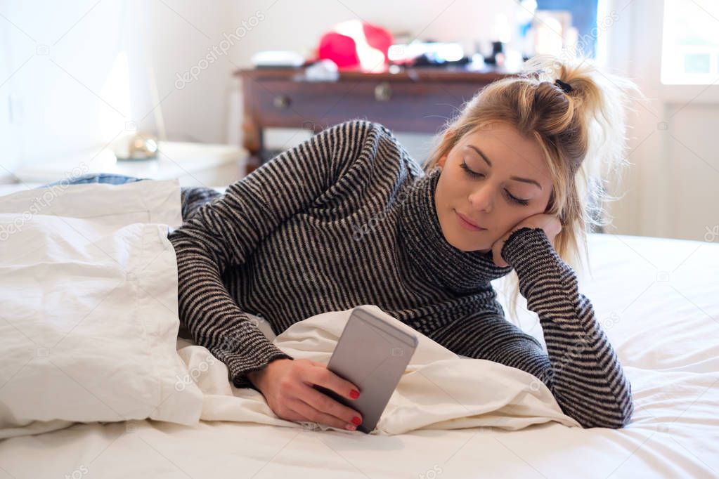 Teenage girl relaxing in bedroom reading phone news feed