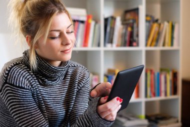 Genç öğrenci e-kitap ve kitaplık arka plan üzerinde kullanma