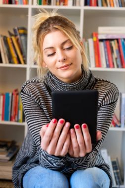 Genç kız e-kitap okuyucu renkli bookshelf yanındaki okuma