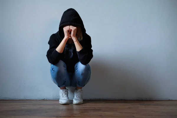 Jong meisje verbergt haar gezicht onder hooded sweatshirt geïsoleerd op b — Stockfoto