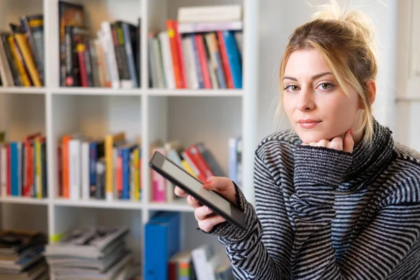 Junge Studentin mit E-Book und Bücherregal im Hintergrund — Stockfoto