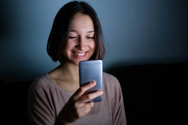 Mulher sorridente usando celular na escuridão à noite — Fotografia de Stock