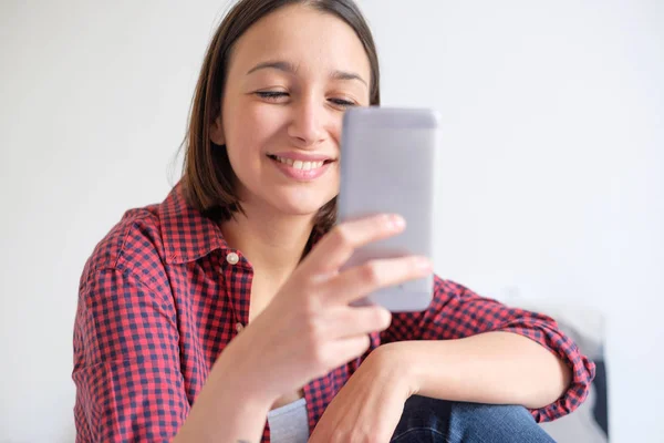 Chica joven sentada en la cama y viendo contenido en el teléfono inteligente — Foto de Stock