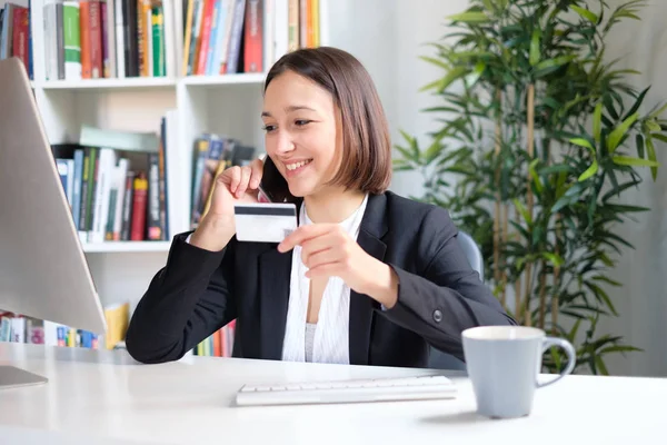 Ung affärskvinna med kreditkort som sitter bakom skrivbordet — Stockfoto