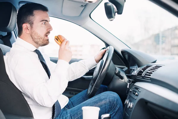 Hombre comiendo comida de engorde y conduciendo sentado en coche — Foto de Stock