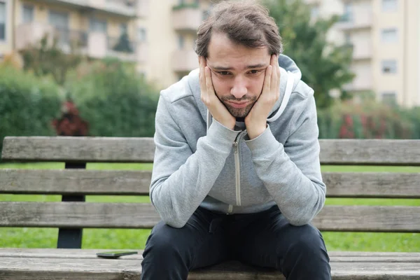 Mannen i bekymmer sitter alla ensam på en bänk i offentlig park — Stockfoto