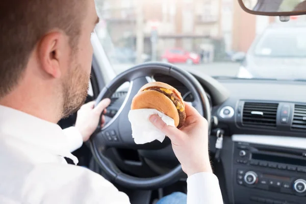 Hombre comiendo comida chatarra y conduciendo sentado en el coche — Foto de Stock