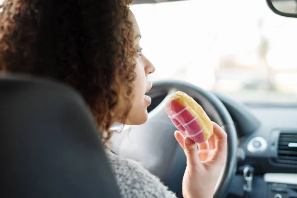 Mujer comiendo un dulce conduciendo un coche — Foto de Stock