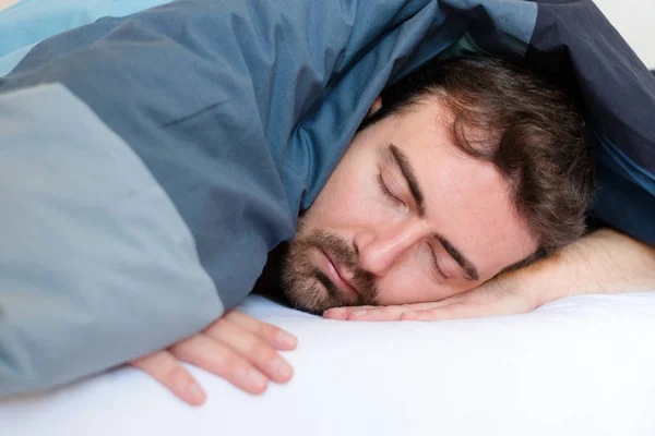 Cansado homem dormindo na cama sob cobertores — Fotografia de Stock