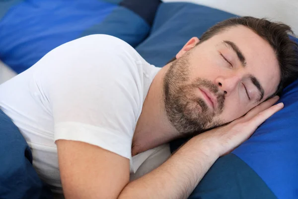 Мирный человек спит под одеялом в постели — стоковое фото