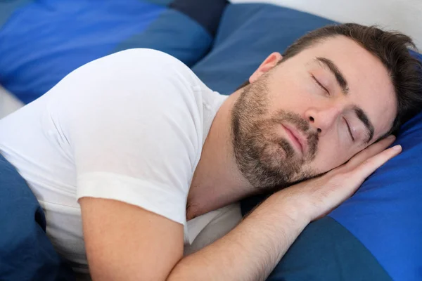 Fredlig man sover under täcker i sängen — Stockfoto