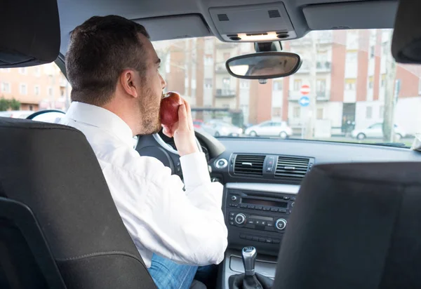 Homme mangeant une pomme voiture de conduite — Photo