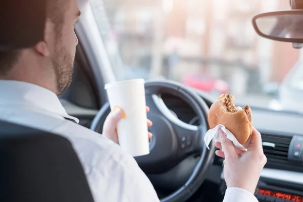 男、ハンバーガーを食べると車に座って運転 — ストック写真