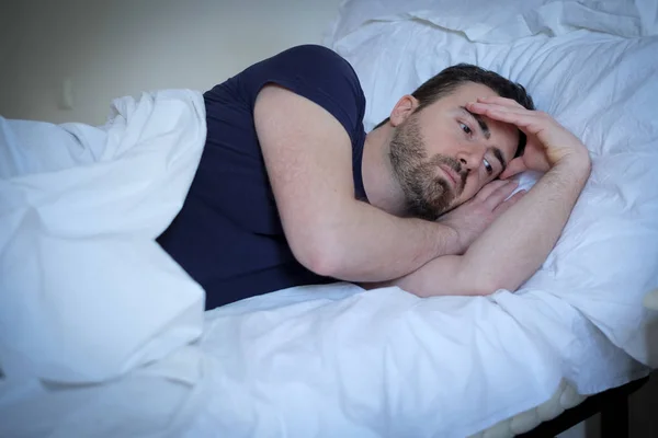 Smutny i zdenerwowany mężczyzna stara się spać w łóżku — Zdjęcie stockowe